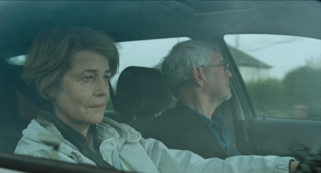 45 Years (2015) movie still: medium — Two individuals sit in the front seats of a moving car during an overcast day. A woman in a light jacket is in…