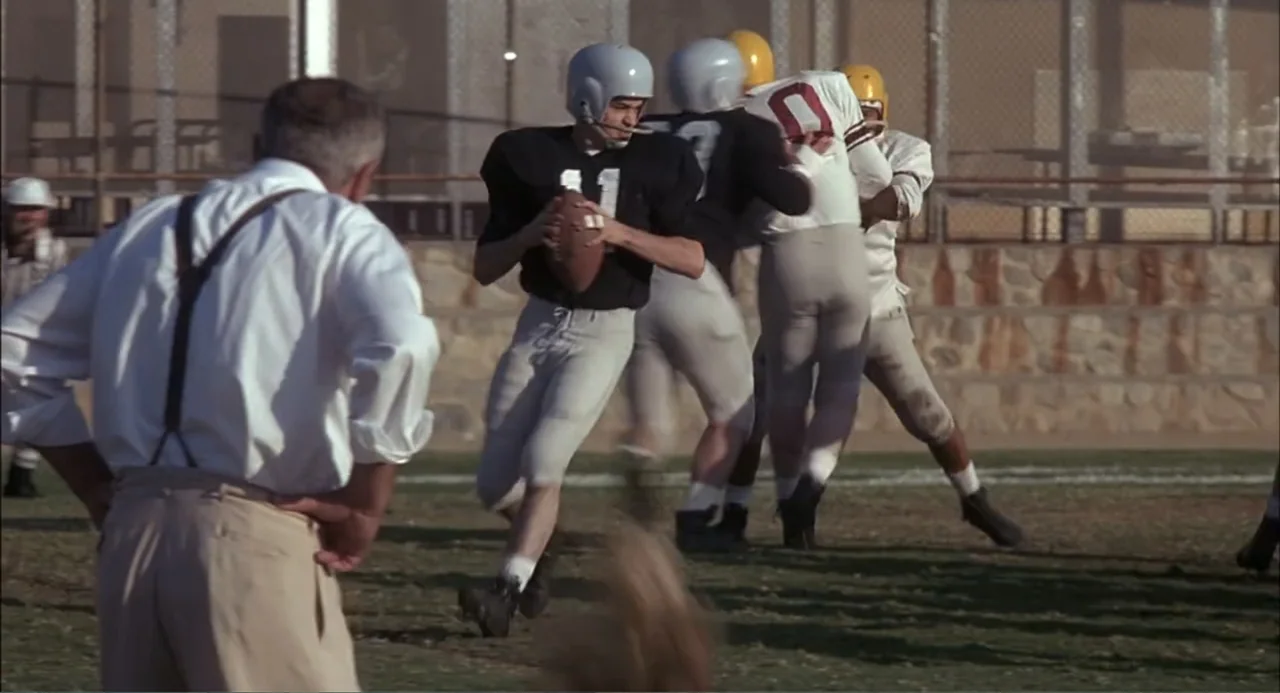 Wild Orchid II: Two Shades of Blue (1991) movie still: medium — A group of football players in 1950s style gear practice on a grass field. An coach…