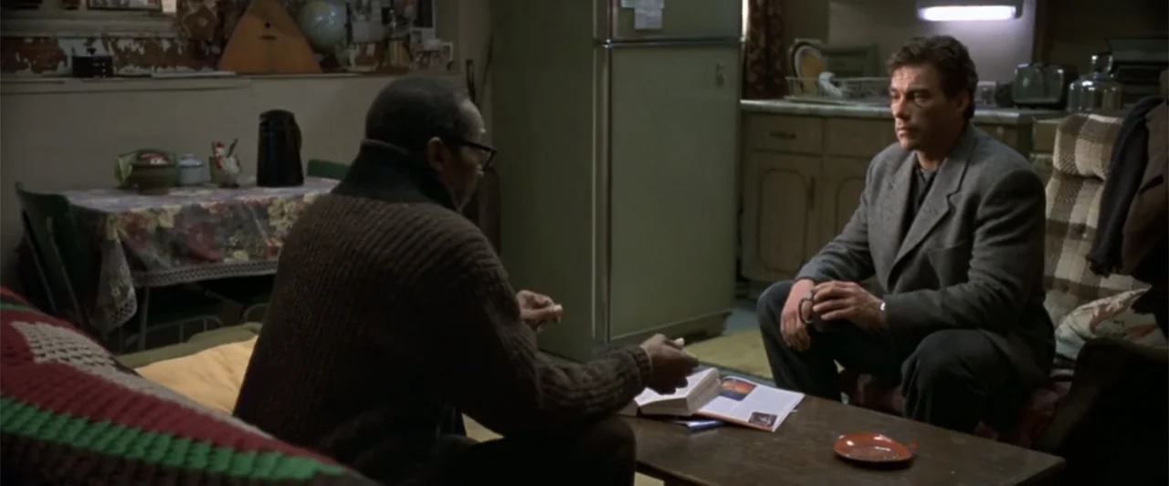 Maximum Risk (1996) movie still: medium — A cluttered apartment interior features an aging refrigerator and a table covered with items. A man in a…