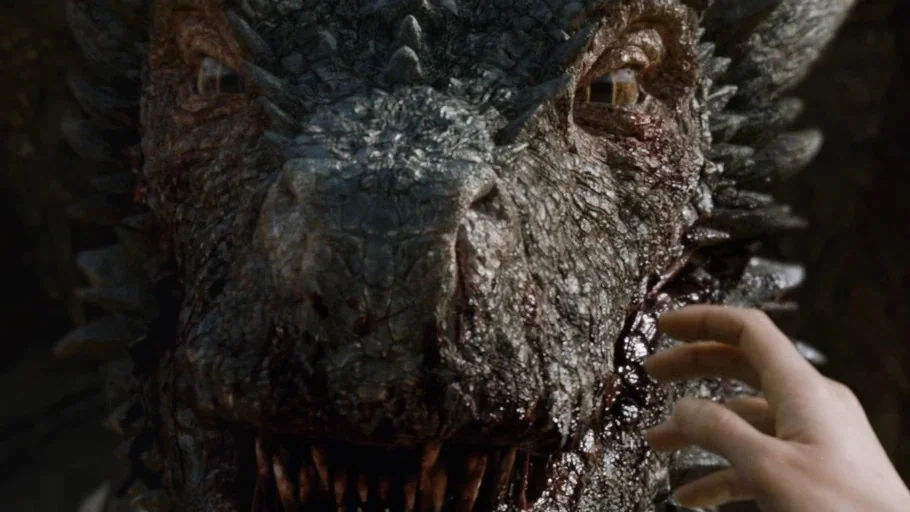 Game of Thrones (2015) movie still: closeup — A close-up shot focuses on the blood-spattered, scaled face of a large dragon. A human hand reaches…