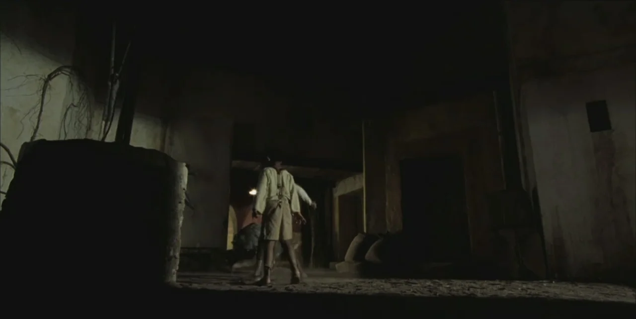 Exorcist: The Beginning (2004) movie still: fullbody — A dark, unfinished room features dirt floors and rough, weathered walls in the shadows. A…