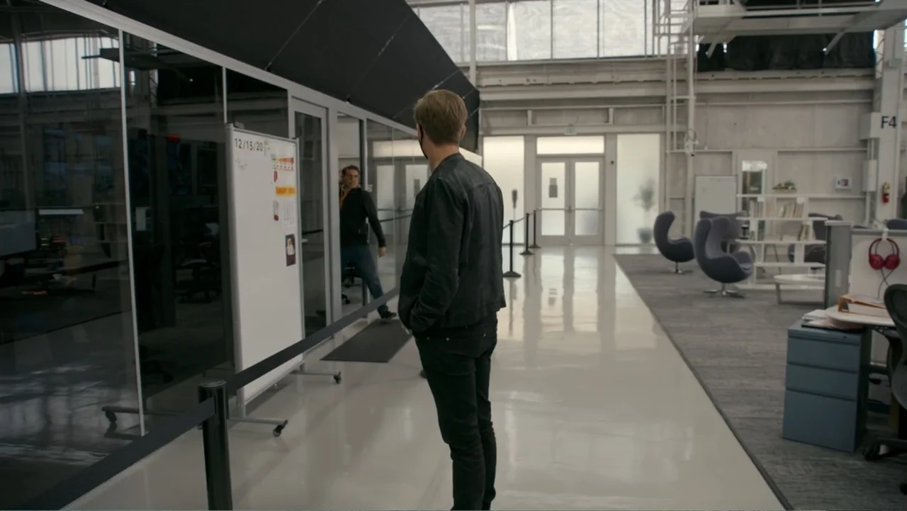 Wild Wild Space (2024) movie still: fullbody — A spacious office interior features white floors and glass-partitioned rooms under high ceilings. A…