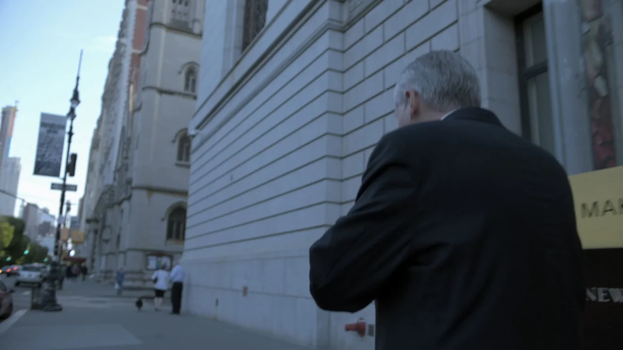 The Soul of America (2020) movie still: medium — A city sidewalk beside a large limestone building with classical architectural features. An older…