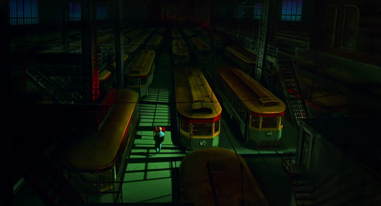 Dick Tracy (1990) movie still: wide — A vast, dark industrial depot houses rows of yellow streetcars under high-contrast artificial lighting. A…