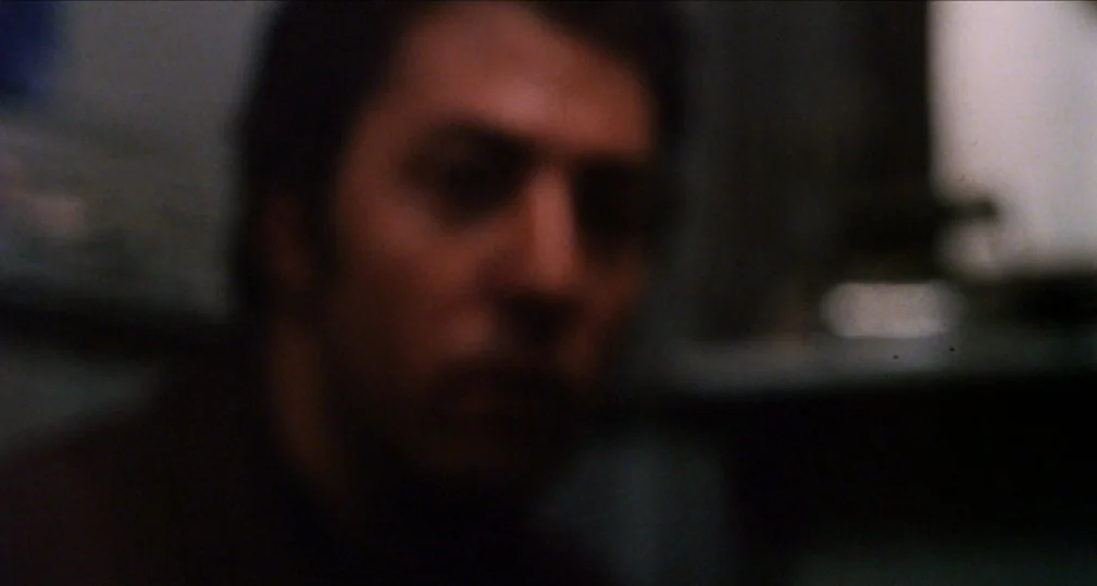 Midnight Cowboy (1969) movie still: closeup — A dimly lit, out-of-focus interior space with minimal architectural detail visible. An unidentified…