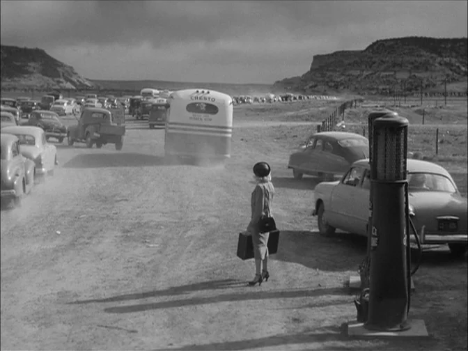 Ace In The Hole (1951) movie still: wide — A dry, dusty roadside in an arid landscape features parked mid-century automobiles. A woman holding a…