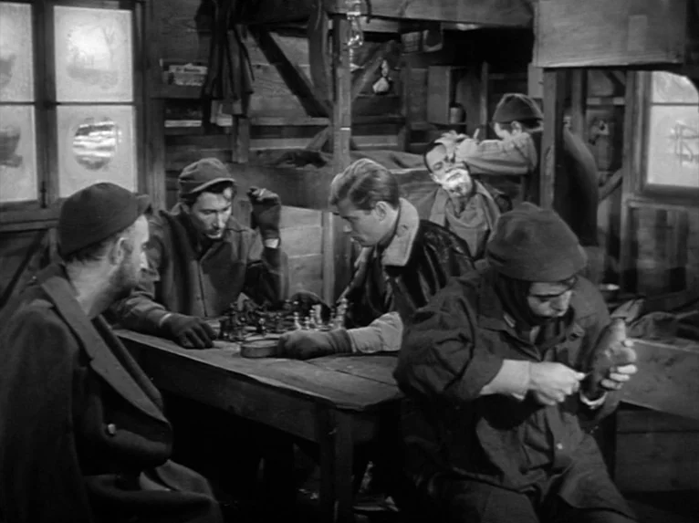 Stalag 17 (1953) movie still: medium — A rustic wooden cabin features bunks in the back and frosted window panes. Several men in dark utilitarian…