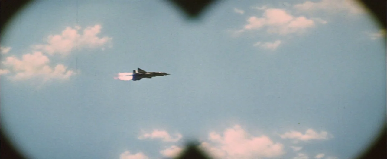 Destroy All Monsters (1968) movie still: wide — A clear blue sky with light clouds is framed through a circular viewfinder. A jet aircraft with a…