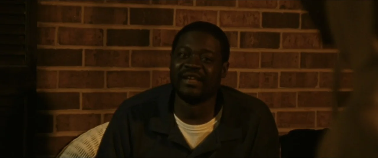 Sermon on the Mount (2019) movie still: medium — A man sits indoors in front of an exposed red brick wall. The subject speaks to an unseen…