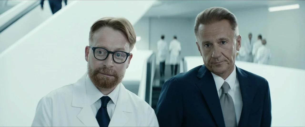 Invasion (2020) movie still: medium — A stark white clinical hallway with modern architectural lines and blurred figures in the distance. A man in a…