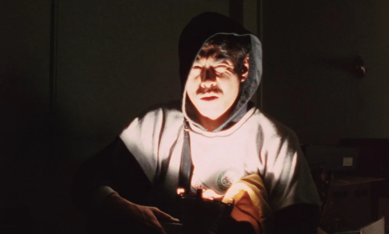Evil Dead Trap (1988) movie still: medium — A dimly lit room holds a man illuminated by a low-positioned light source. The subject sits facing the…
