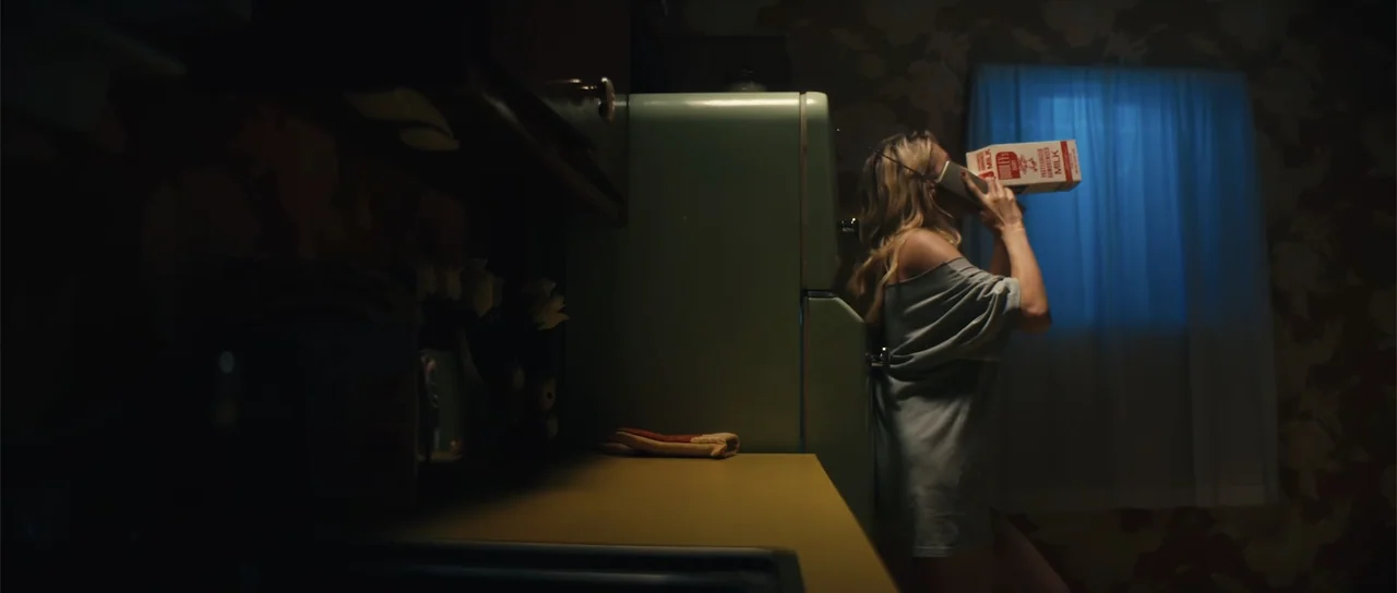 Night of the Missing (2023) movie still: medium — A dark kitchen features a retro mint green refrigerator and floral wallpaper near a window. A…