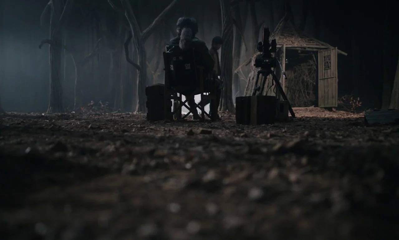Cobweb (거미집) (2023) movie still: wide — A dark, misty woodland clearing contains a wooden shack and production equipment in the center. A person…