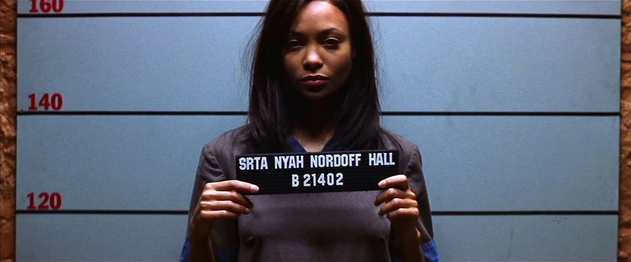 Mission: Impossible II (2000) movie still: medium — A mugshot backdrop with height markers features a blue-grey wall surface. A woman stands in…
