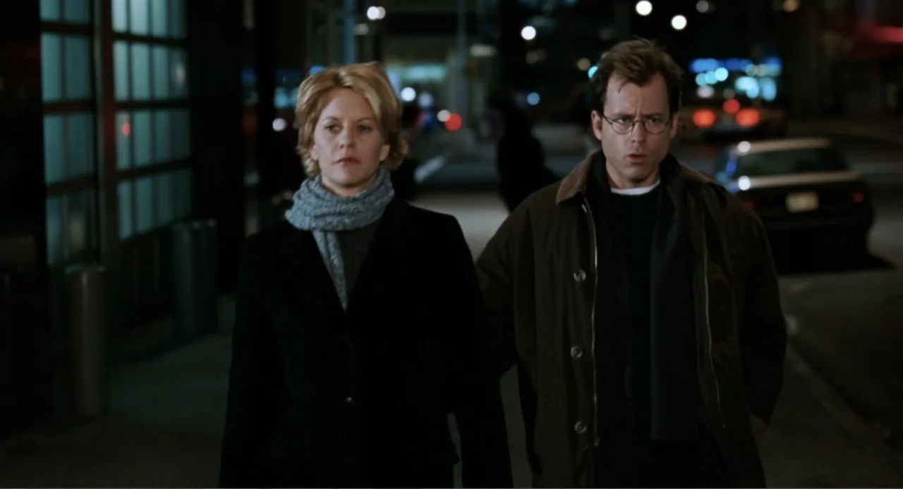 You've Got Mail (1998) movie still: medium — A dark city street at night features blurred lights and a parked car background. A man and a woman walk…