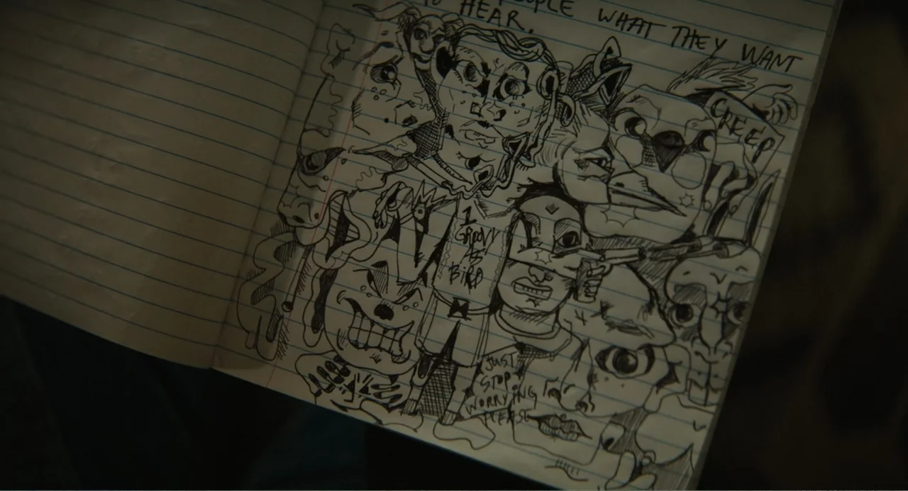 Beautiful Boy (2011) movie still: closeup — A notebook page contains dense black ink illustrations of various faces and figures. Hand-written text…