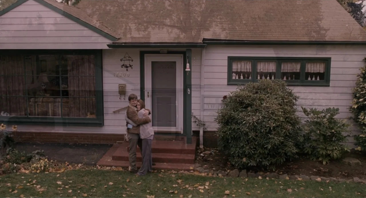 Management (2009) movie still: fullbody — A single-story suburban house features white siding, a dark roof, and a front porch. A man and a woman…