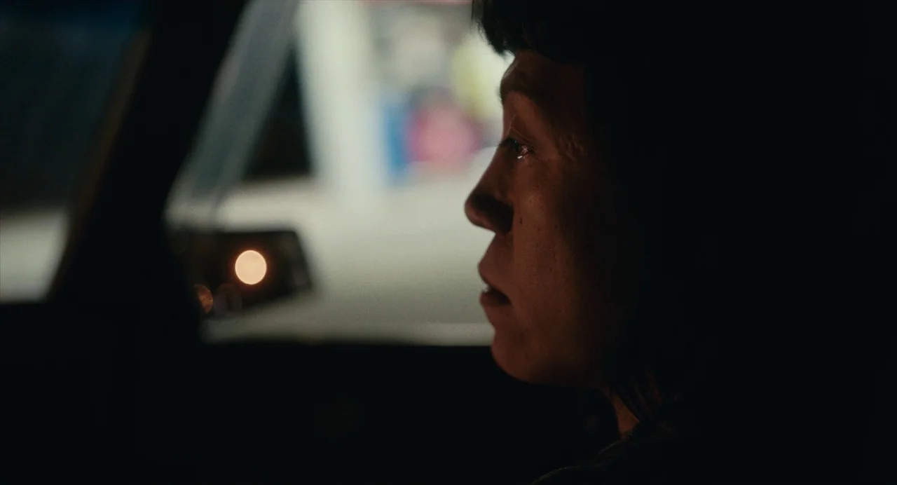 Lingua Franca (2019) movie still: closeup — The interior of a dark car at night looking out toward a blurred city street. A woman sits in the driver…