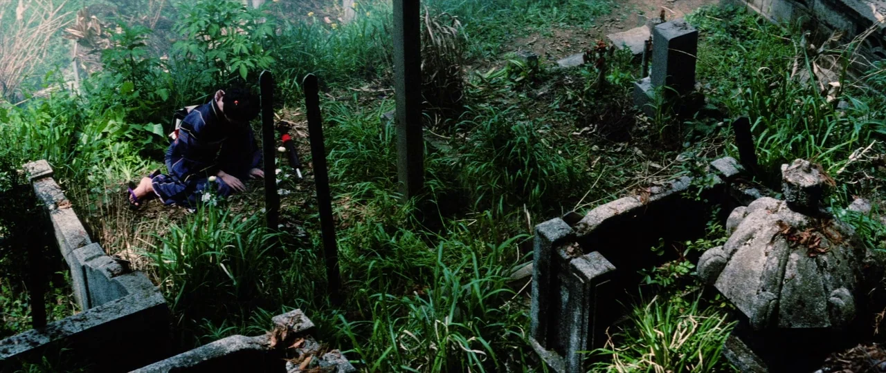 Lady Snowblood Song of Vengeance (1974) movie still: wide — An overgrown cemetery features weathered stone markers nestled among wild tall grass and…