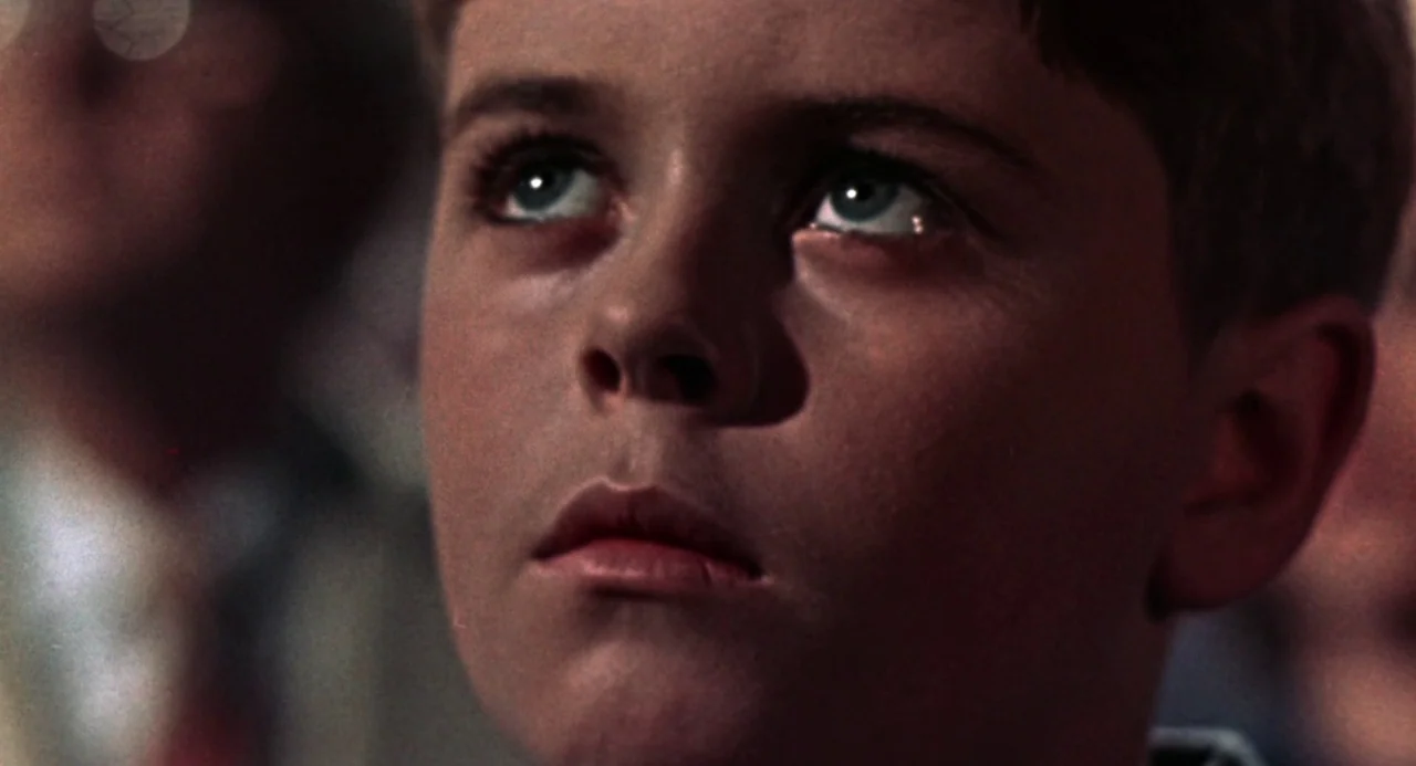 Queen of Blood (1966) movie still: closeup — The face of a young boy is illuminated in a darkened room. He gazes upward with wide eyes while others…