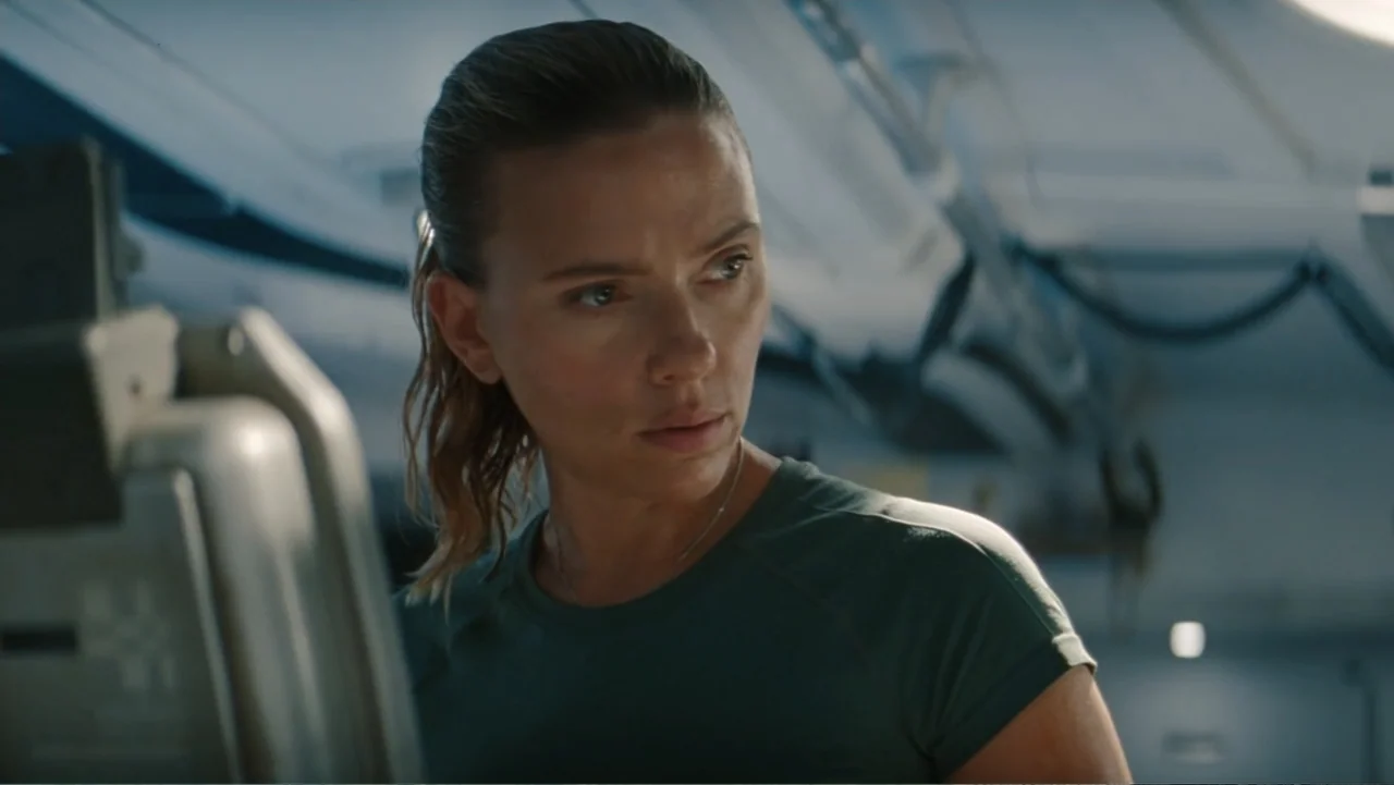 Jurassic World Rebirth (2025) movie still: medium — The interior of a high-tech aircraft cabin features curved white walls and equipment. A woman…