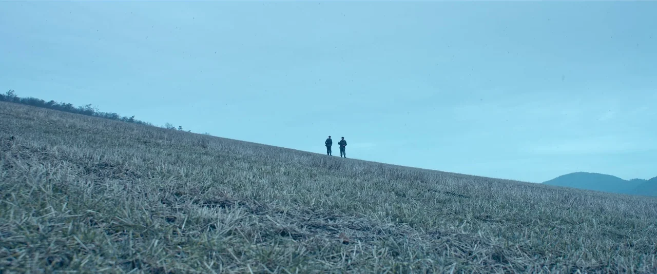 All Quiet on the Western Front (2022) movie still: wide — A vast, harvested agricultural field stretches toward a distant ridge under a pale sky.…