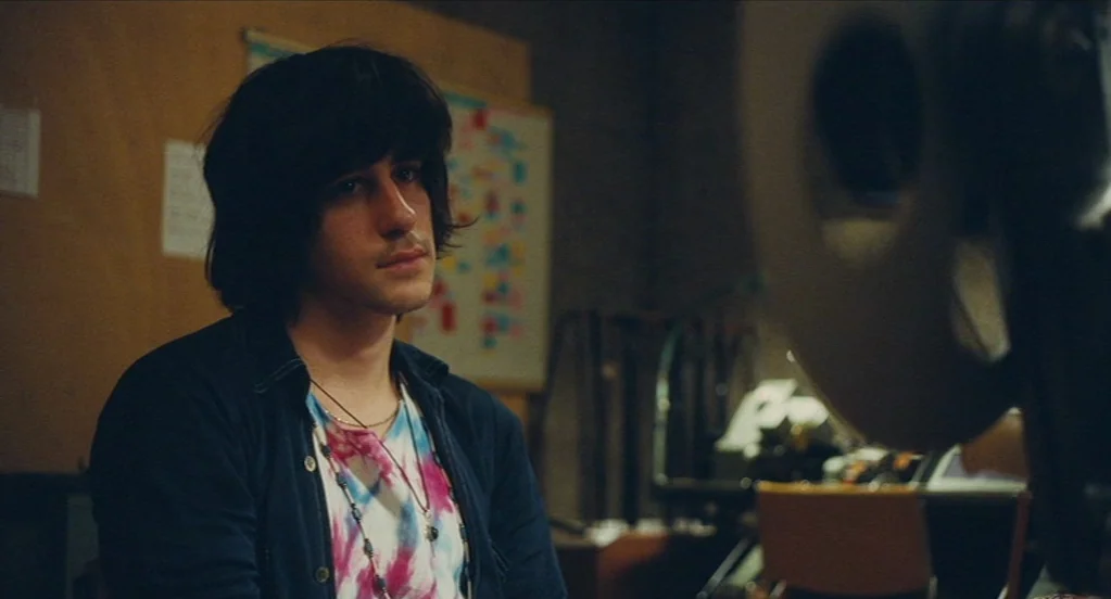 Something in the Air (2012) movie still: medium — A basement space with a notice board on the wall and technical equipment. A young man with…