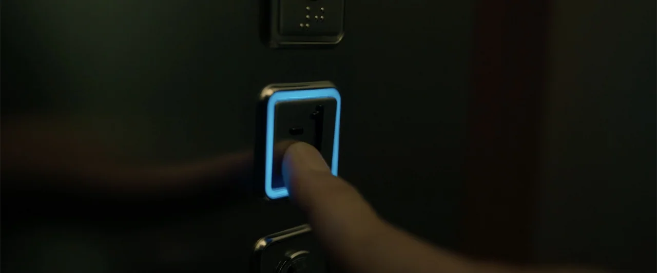Den of Thieves 2: Pantera (2025) movie still: closeup — A close-up view shows a finger interacting with the metallic panel of an elevator. The…