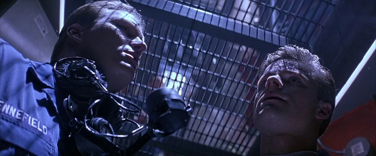 Crimson Tide (1995) movie still: medium — A dimly lit interior with a metal grating overhead and industrial pipes visible. Two men in work uniforms…