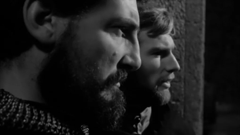 Falstaff (Chimes at Midnight) (1965) movie still: closeup — Two men with beards stand against a rough stone surface at night. They look toward the…