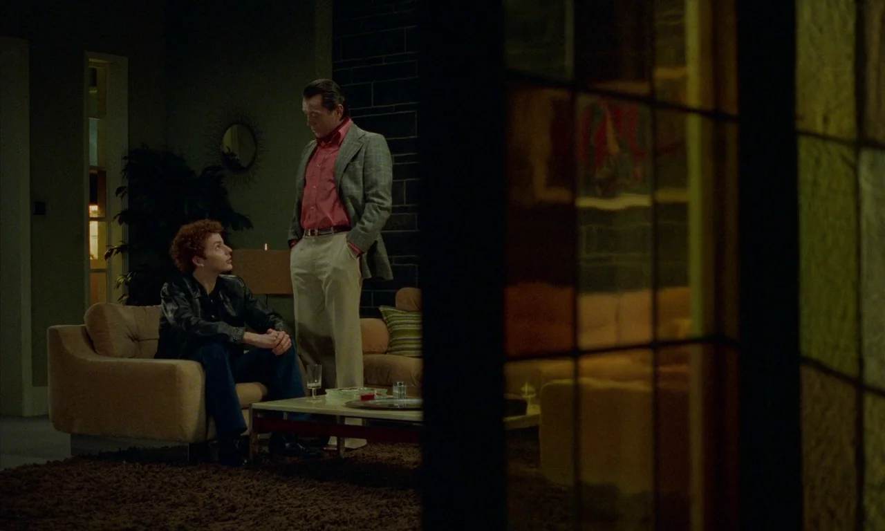 Water Drops on Burning Rocks (2000) movie still: medium — A 1970s living room features a dark brick accent wall and brown shag carpet. A young man…