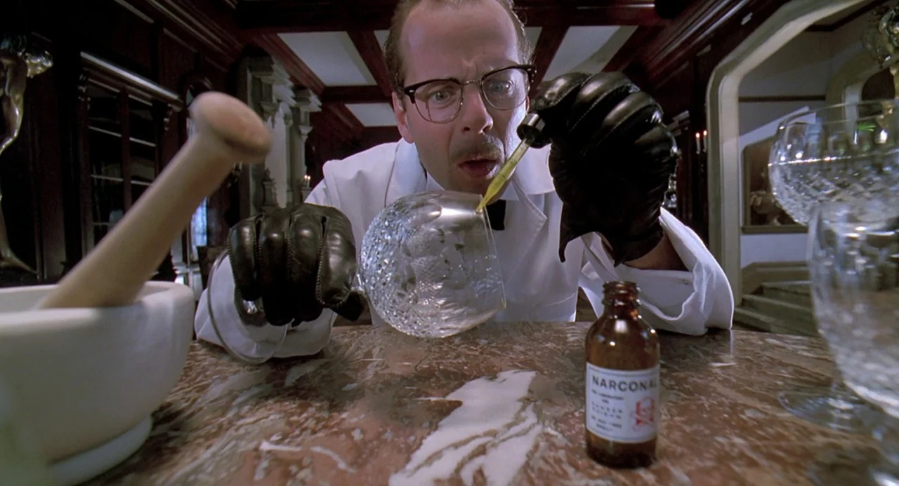 Death Becomes Her (1992) movie still: medium — A dark wood-paneled room contains a polished marble table holding chemicals and glasses. A man in…