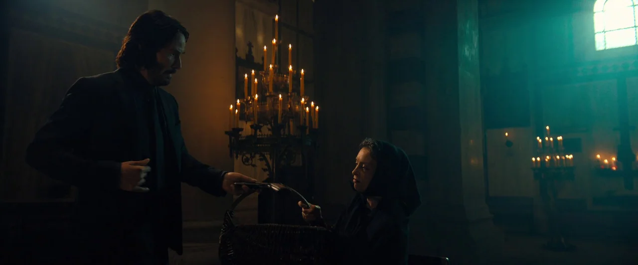 John Wick: Chapter 4 (2023) movie still: medium — A dark church interior with heavy shadows and multiple burning candle stands. A man in a suit…