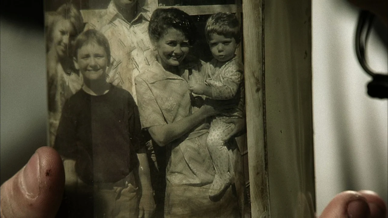 The Texas Chainsaw Massacre (2003) movie still: closeup — A hand holds a physical photograph containing a group portrait of four people. The…
