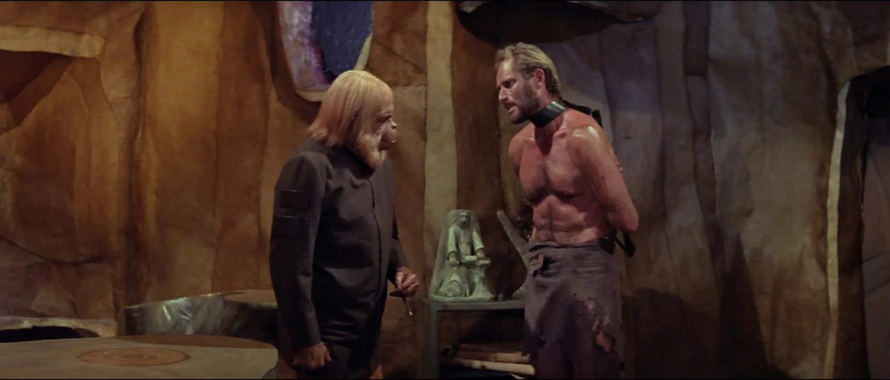 Planet of the Apes (1968) (1968) movie still: medium — A stone-walled interior resembles a rustic cavern with textured rock surfaces. A costumed ape…