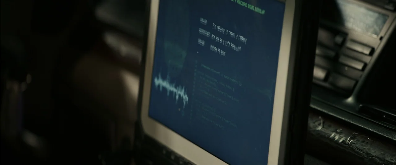 Hypnotic (2023) movie still: closeup — A dark vehicle cabin features a rugged laptop screen displaying blue text and waveforms. The screen light…