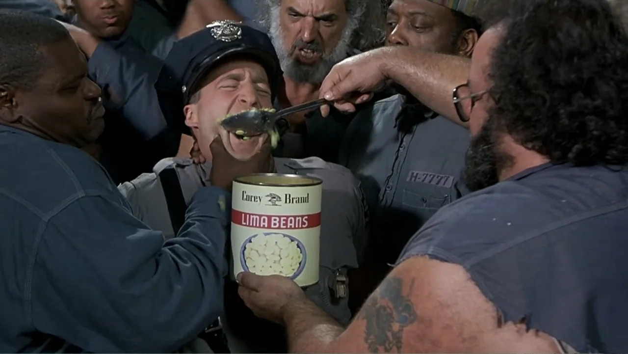 Naked Gun 33⅓: The Final Insult (1994) movie still: medium — An indoor prison environment where several inmates surround a police officer. The men…