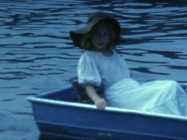 Der Bomberpilot (1970) movie still: medium — A teenage girl sits in a small blue rowboat on dark, rippling water. She looks toward the camera while…