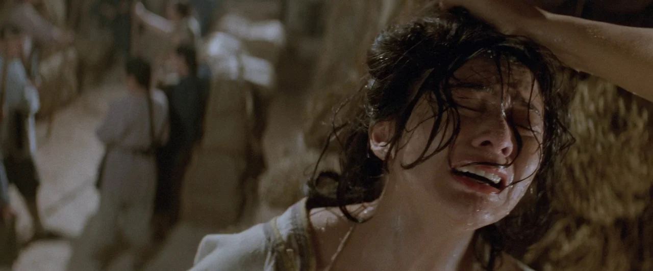 Once Upon a Time in China (1991) movie still: closeup — A dimly lit room with blurred figures standing in the background. A woman's head is held…