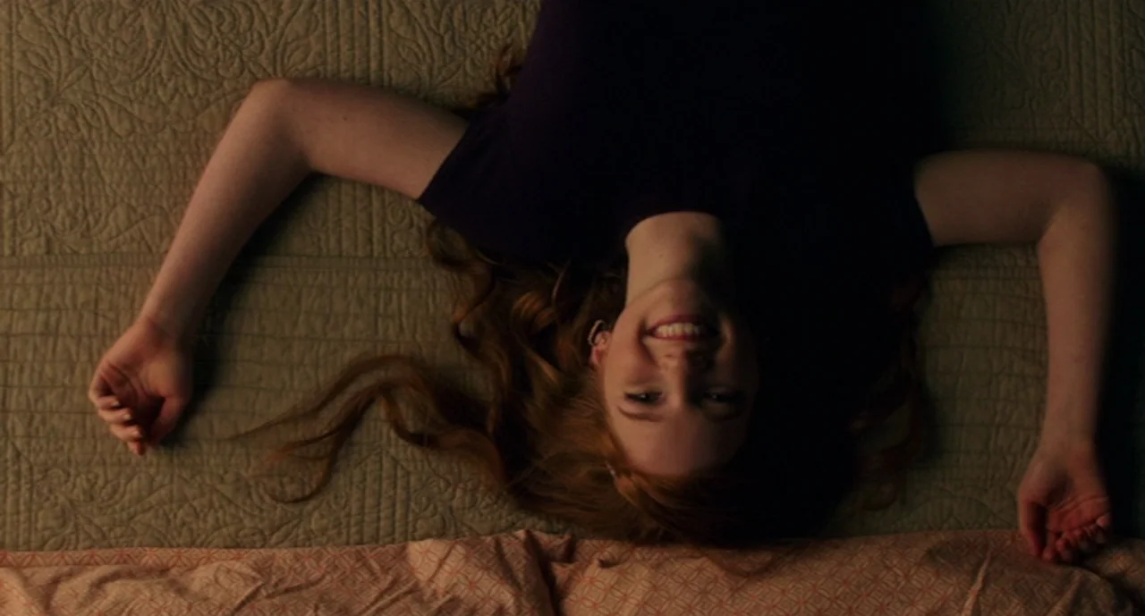 Ouija: Origin of Evil (2016) movie still: medium — A person lies on a textured, quilted olive-green bedspread. The person is looking upward toward…