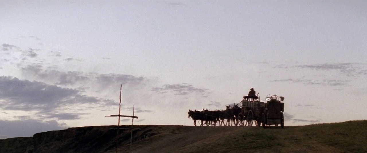 Dances With Wolves (1990) movie still: wide — A horse-drawn wagon travels across a desolate, grass-covered ridge at twilight. A single figure sits…
