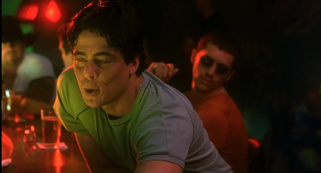 Traffic (2000) movie still: medium — A dark, neon-lit bar features two men standing near a polished wooden surface. The man in the foreground gazes…