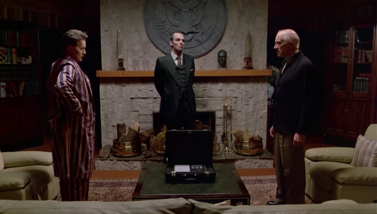 The Dead Zone (1983) movie still: wide — A wood-paneled room contains a central fireplace with a large carved eagle emblem above. Three men stand…