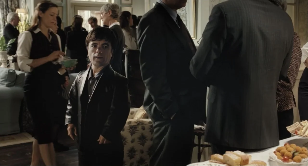 Death at a Funeral (2010) movie still: medium — A well-lit indoor gathering features several people standing in a room with light-colored walls. A…