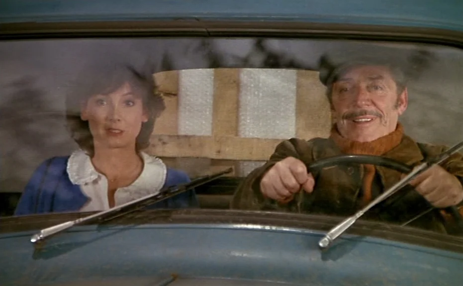 Life Is A Bed of Roses (1983) movie still: medium — The interior of a blue vintage car is visible through the front windshield glass. A man drives…