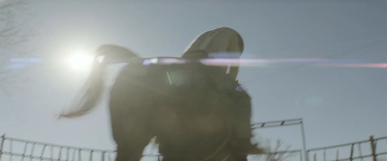 Cry Macho (2021) movie still: medium — An outdoor fenced enclosure is visible under a clear, bright sky. A person riding a horse moves across the…