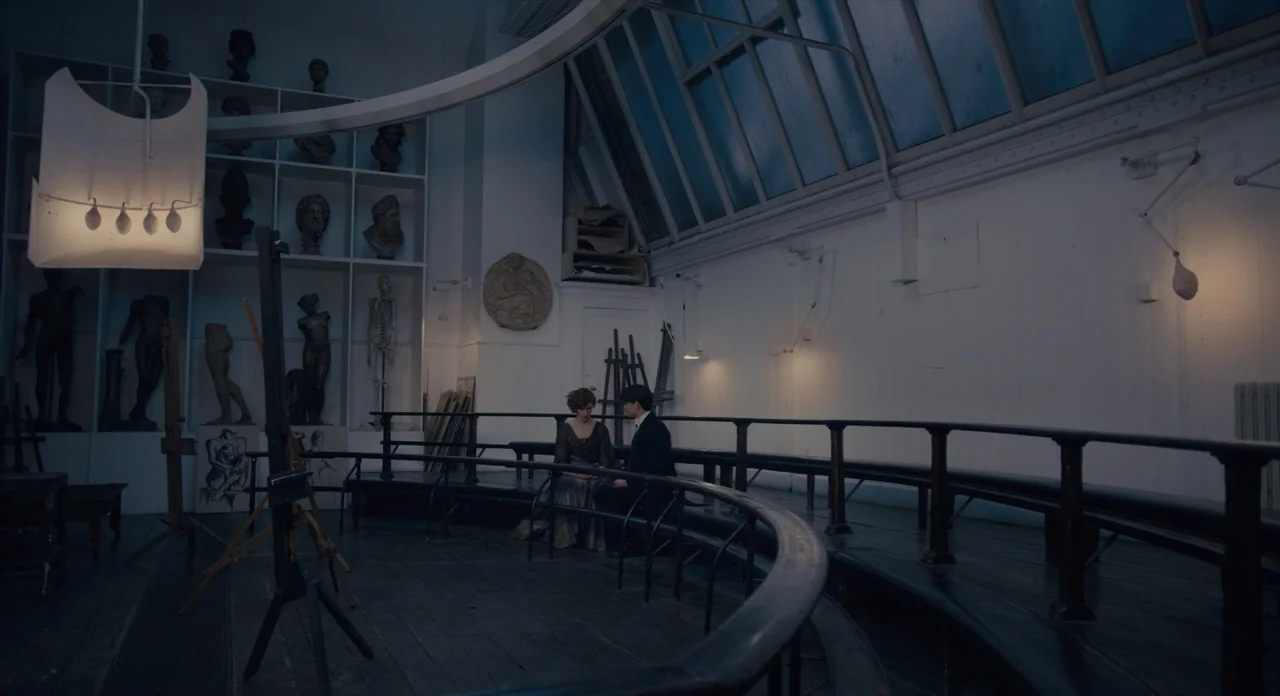 The Danish Girl (2015) movie still: wide — An art classroom features tiered wooden seating, numerous anatomical busts, and a high skylight. A man…