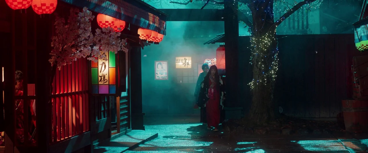Prisoners of the Ghostland (2021) movie still: wide — A narrow Japanese style walkway filled with teal smoke and red hanging lanterns. A woman in a…