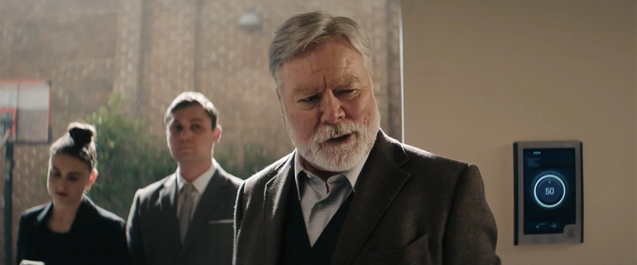 M3GAN 2.0 (2025) movie still: medium — An interior office space with a digital display showing a number on the wall. Three people stand together…