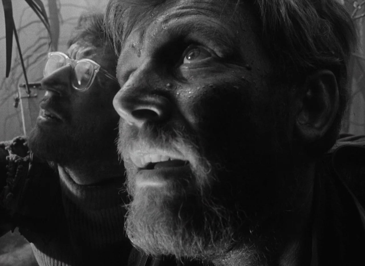 Letter Never Sent (1960) movie still: closeup — Two bearded men with dirt-covered faces look toward the sky in an open field. The lighting is harsh…